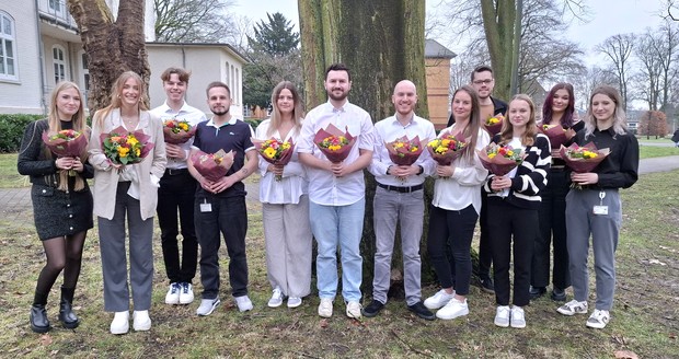 Schülerinnen und Schüler stehen nach bestandenem Examen mit bunten Blumensträußen in der Hand im Halbkreis.